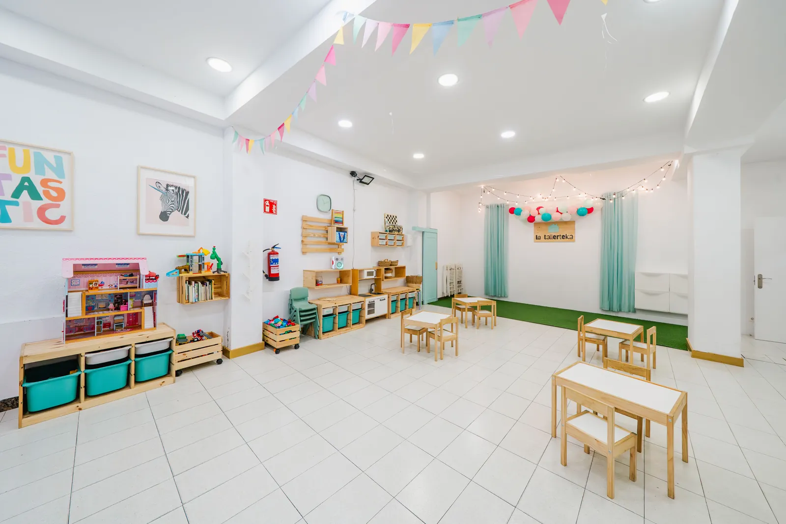 Sala de actividades de La Tallerteka con banderines de colores y mesas infantiles